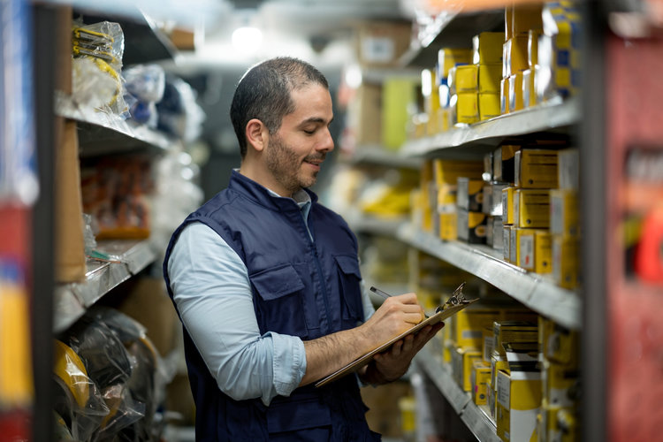 Employee with clipboard checking critical parts storage in warehouse